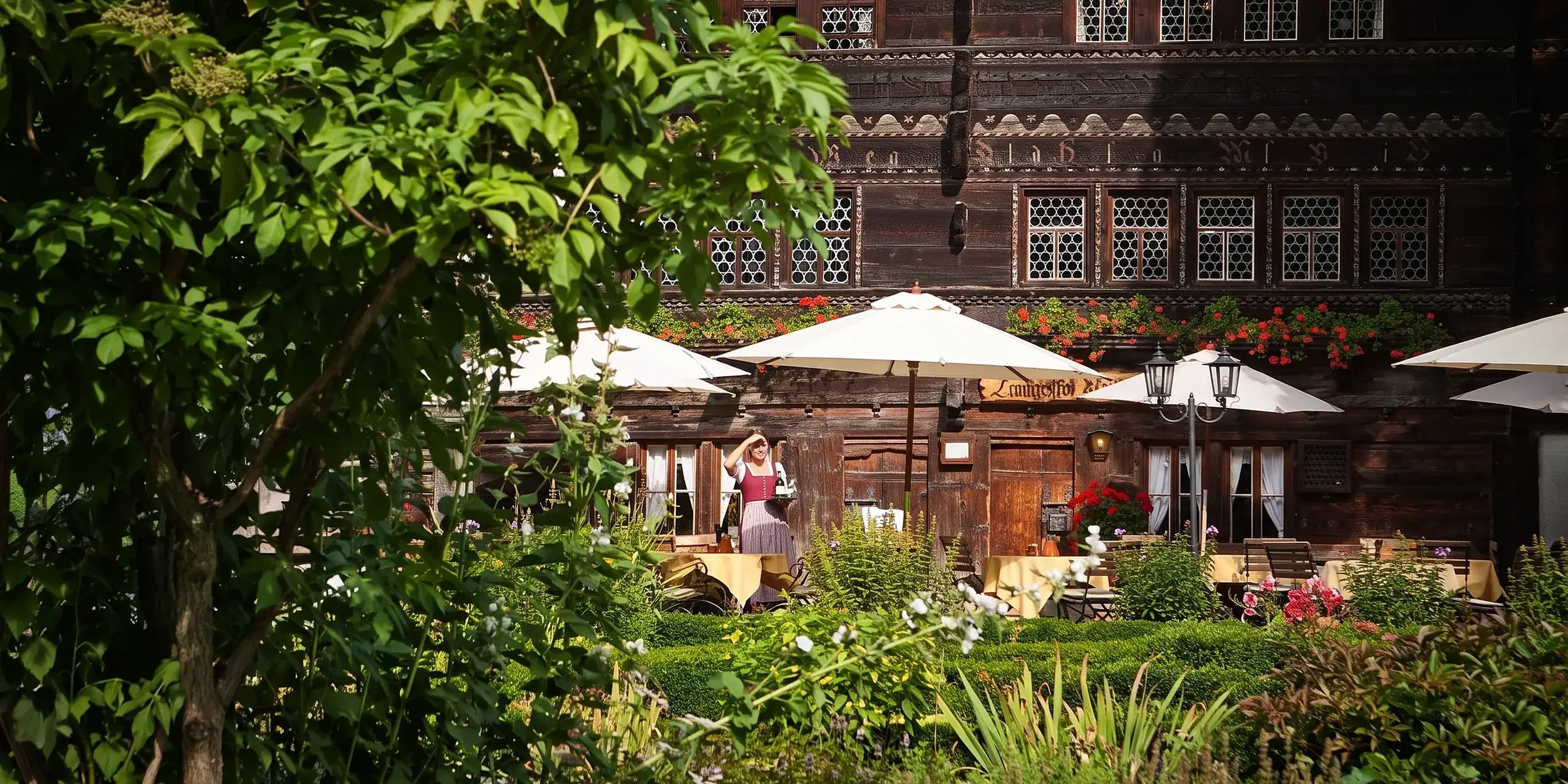 Der Landgasthof Ruedihus in Kandersteg hinter Laub, davor die Terrasse mit den Schirmen